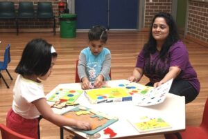 A lady teacher is teaching arts to the small kids.
