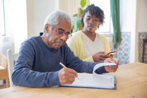 A caregiver is helping an old man in writing, designing.