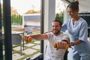A caregiver is helping a man sitting in a wheelchair to do a physical therapy as part of NDIS services.